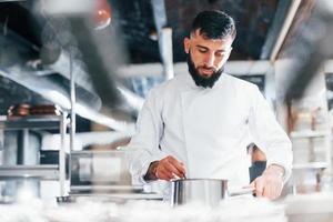 Koch in weißer Uniform, der Essen in der Küche kocht. arbeitsreicher Tag foto