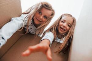 Blick in die Papierschachtel. Zwei süße kleine Mädchen drinnen zu Hause zusammen. Kinder haben Spaß foto