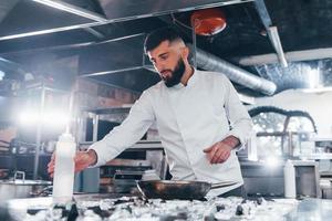 verwendet Bratpfanne. Koch in weißer Uniform, der Essen in der Küche kocht. arbeitsreicher Tag foto