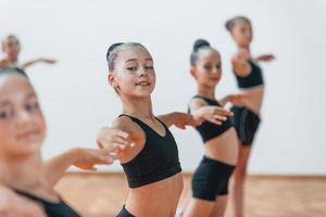 stehen und synchronisierte Bewegungen ausführen. Gruppe weiblicher Kinder, die gemeinsam Sportübungen im Innenbereich praktizieren foto