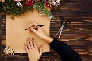 Frau schreibt auf Papier. Draufsicht der festlichen Weihnachtsbeschaffenheit mit Dekorationen des neuen Jahres foto