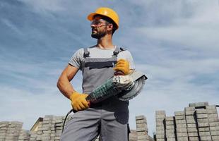 posieren für eine Kamera mit Kreissäge. männliche arbeiter in gelber uniform haben arbeit mit pflaster foto