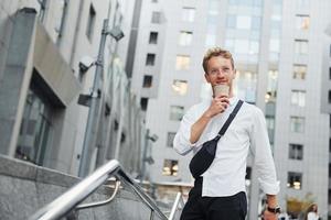 macht eine Pause. in den Händen trinken. junger eleganter mann in guter kleidung ist tagsüber draußen in der stadt foto