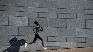 Seitenansicht einer jungen Afroamerikanerin in sportlicher Kleidung, die in der Nähe der Wand verläuft foto
