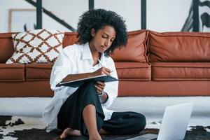 mit Laptop. junge afroamerikanische frau mit lockigem haar drinnen zu hause foto