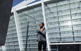 großes Gebäude dahinter. junge afroamerikanerin in sportlicher kleidung trainiert tagsüber im freien foto