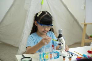 bildung, wissenschaft und kinderkonzept - mädchen in schutzbrillen, die reagenzglas mit chemikalien zu hause untersuchen foto