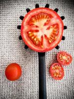 halbe tomate auf einem gezahnten küchenlöffel auf grauem grund. vertikales Bild. foto