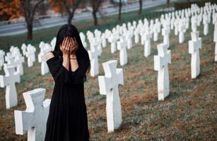 junge Frau in schwarzer Kleidung, die den Friedhof mit vielen weißen Kreuzen besucht. Vorstellung von Begräbnis und Tod foto