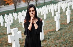 junge Frau in schwarzer Kleidung, die den Friedhof mit vielen weißen Kreuzen besucht. Vorstellung von Begräbnis und Tod foto