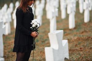 Partikelansicht. junge Frau in schwarzer Kleidung, die den Friedhof mit vielen weißen Kreuzen besucht. Vorstellung von Begräbnis und Tod foto