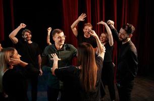 glückliche menschen, die erfolg feiern. Gruppe von Schauspielern in dunkler Kleidung bei der Probe im Theater foto