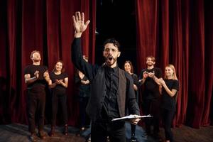 Mann übt seine Rolle. Gruppe von Schauspielern in dunkler Kleidung bei der Probe im Theater foto