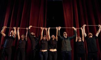 Seil in den Händen über den Köpfen halten. Gruppe von Schauspielern in dunkler Kleidung bei der Probe im Theater foto