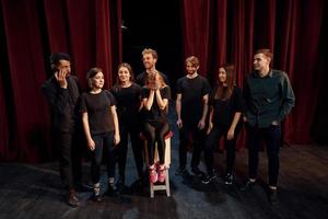 Mädchen sitzt auf Stuhl und weint. Gruppe von Schauspielern in dunkler Kleidung bei der Probe im Theater foto