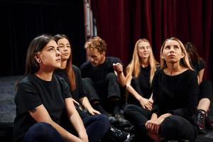 auf dem Boden sitzen. Gruppe von Schauspielern in dunkler Kleidung bei der Probe im Theater foto