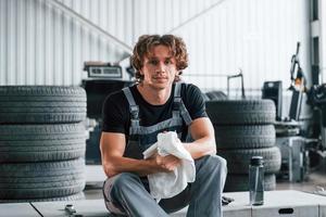 sitzen und Hände abwischen. erwachsener mann in grauer uniform arbeitet im autosalon foto