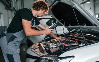 testet die Elektronik des Autos. erwachsener mann in grauer uniform arbeitet im autosalon foto