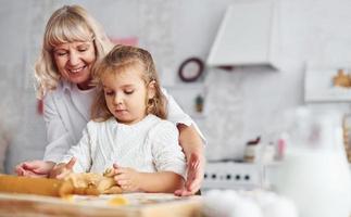 knetet den Teig. senior großmutter mit ihrer kleinen enkelin kocht süßigkeiten zu weihnachten in der küche