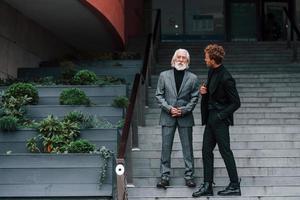 auf der Treppe gehen. junger mann mit senior in eleganter kleidung ist zusammen im freien. Geschäftskonzept foto