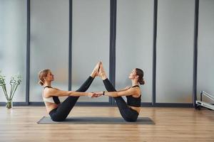 Gleichgewichtsübungen machen. zwei frauen in sportlicher kleidung und mit schlanken körpern haben zusammen einen fitness-yoga-tag drinnen foto