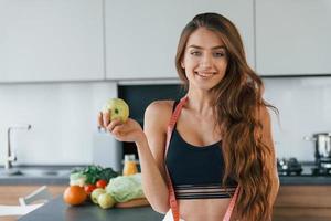 hält Apfel in der Hand. junge europäerin ist drinnen in der küche drinnen mit gesundem essen foto