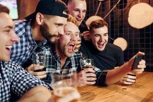 verwendet Telefon. gruppe von menschen zusammen drinnen in der kneipe haben spaß am wochenende foto