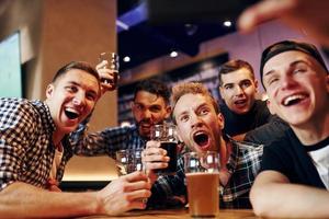 Mann macht Selfie per Telefon. gruppe von menschen zusammen drinnen in der kneipe haben spaß am wochenende foto