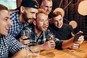 verwendet Telefon. gruppe von menschen zusammen drinnen in der kneipe haben spaß am wochenende foto