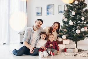 sitzt gegen Tanne. schöne familie feiert neujahr und weihnachten zuhause zu hause foto