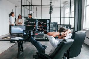 mann sitzt auf stuhl und macht pause. Das Team von Börsenmaklern arbeitet in einem modernen Büro mit vielen Bildschirmen foto