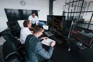 hält Dokument in Händen. Das Team von Börsenmaklern arbeitet in einem modernen Büro mit vielen Bildschirmen foto