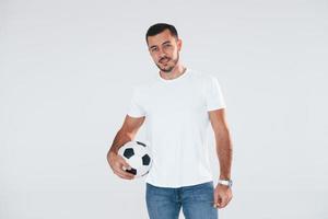 Fußballfan mit Fußball. junger gutaussehender Mann, der drinnen vor weißem Hintergrund steht foto