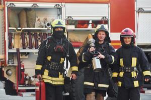 Gruppe von Feuerwehrleuten in Schutzuniform, die sich im Freien in der Nähe eines Lastwagens befinden foto