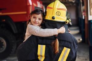 glückliches kleines mädchen ist mit feuerwehrfrau in schutzuniform foto