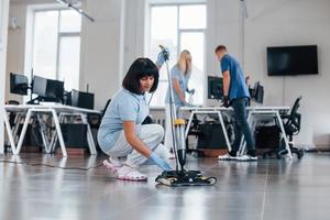 Frau benutzt Staubsauger. gruppe von arbeitern reinigt tagsüber gemeinsam ein modernes büro foto