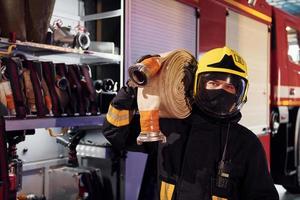 hält Schlauch. männlicher feuerwehrmann in schutzuniform, der in der nähe von lkw steht foto