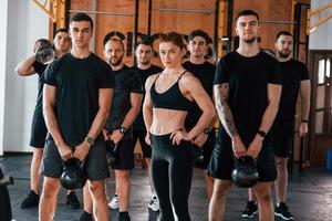 für eine Kamera posieren. eine gruppe junger sportlicher leute hat drinnen im fitnessstudio einen crossfit-tag foto