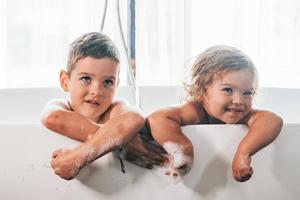 Zwei Kinder haben Spaß und waschen sich zu Hause in der Badewanne. für eine Kamera posieren foto