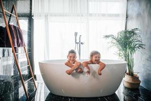 Zwei Kinder haben Spaß und waschen sich zu Hause in der Badewanne. für eine Kamera posieren foto