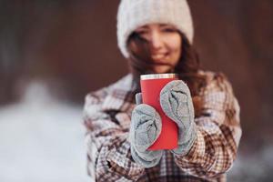 Schöne Frau in warmer Kleidung macht einen Spaziergang im Winterwald. mit Getränk
