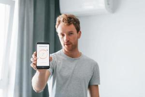 junger mann in lässiger kleidung steuert drinnen die smart-home-technologie foto