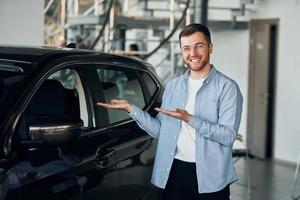 erfolgreicher mann mit brille, der drinnen in der nähe eines brandneuen autos steht foto