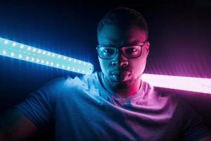 hält Beleuchtungsgeräte. futuristische neonbeleuchtung. junger Afroamerikaner im Studio foto