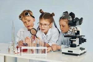 Kinder in weißen Mänteln spielen einen Wissenschaftler im Labor, indem sie Geräte verwenden foto