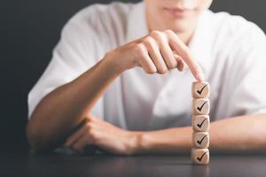 männliche hand, die auf einen holzblock zeigt, häkchensymbol, checklistenkonzept, erhebungskonzepte durch fragebögen, kommentare zur leitung der entwicklung und debugging, ausdruck der zufriedenheit foto