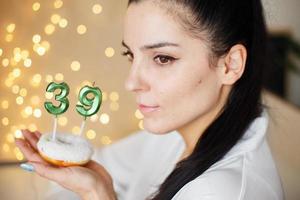 frau, die einen kuchen mit den kerzen der nummer 39 auf festlichem unscharfem bokeh-hintergrund hält foto