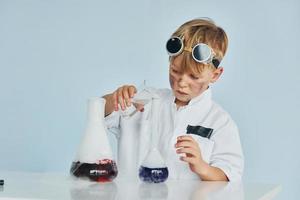 kleiner junge im mantel, der einen wissenschaftler im labor spielt, indem er ausrüstung verwendet foto