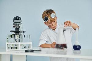 kleiner junge im mantel, der einen wissenschaftler im labor spielt, indem er ausrüstung verwendet foto