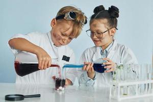 Kleines Mädchen und Junge in weißen Mänteln spielen einen Wissenschaftler im Labor, indem sie Geräte verwenden foto